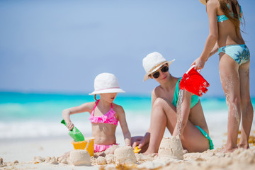 Family of mom and kids making sand castle at tropical beach