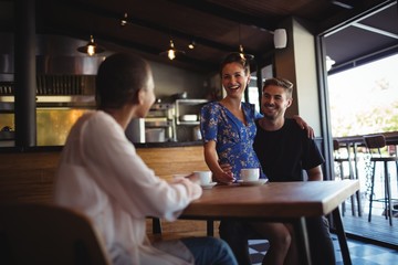 Wall Mural - Friend interacting with happy couple while having coffee