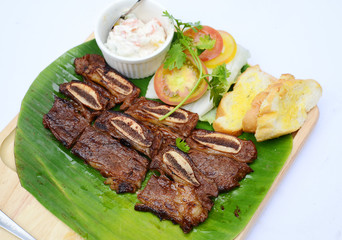 Wall Mural - Grilled chopped pork ribs with bread and tomatoes on banana leaf tray