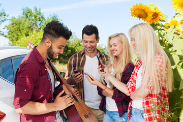 Sticker - Young people listening guy playing guitar friends drinking beer bottles outdoor countryside, two couple standing near car happy smile summer sunflower