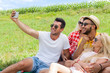 © mast3r - Friends taking selfie photo smart phone picnic countryside young people group sitting blanket outdoor green grass two couple summer sunny day