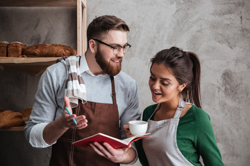 Sticker - Happy loving couple bakers drinking coffee looking at notebook.