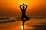Fototapeta Fototapety z morzem do Twojej sypialni - Kobieta ćwicząca jogę na plaży przy zachodzie słońca