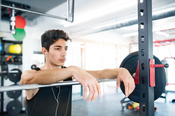 Wall Mural - Hispanic man in gym resting, earphones in his ears,listening mus