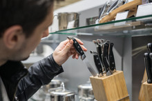 Close Up View Of Customer's Hand Choosing Set Of Knives For Kitchen. He Is Putting Away One Knife