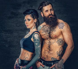 Wall Mural - Studio portrait of full body tattooed couple over dark grey background.