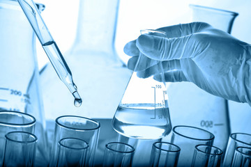Wall Mural - flask in scientist hand with lab glassware background