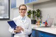 © LIGHTFIELD STUDIOS - Smiling young scientist in eyeglasses holding clipboard in research laboratory