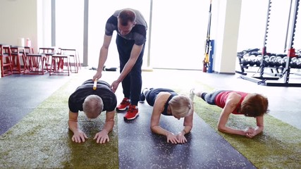 Wall Mural - Fit seniors in gym in plank position with their trainer