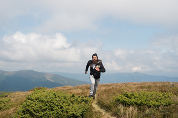 man runs on green meadow in mountain on cloudy sky