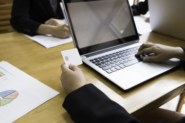 lady co worker using laptop and hold card in hand in work area and office with sheet on wood table and team.