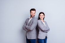 Concept Of Partnership In Business. Young Man And Woman Standing Back-to-back With Crossed Hands Against Gray Background