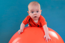 Cute Baby Lying On The Orange Fitball On The Blue Background. Concept Of Caring For The Baby's Health.