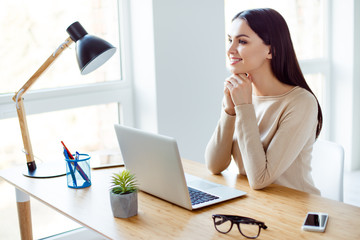 Pretty young woman pordering about successful career sitting at the table and working with laptop