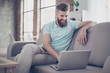 © deagreez - Young bearded man is making shopping online sitting at home on the cozy sofa