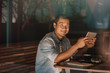 © mavoimages - Smiling Asian man browsing online while sitting in a cafe