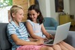 © WavebreakMediaMicro - Smiling siblings interacting while using laptop in living room