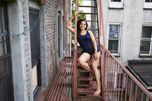 Portrait Of Smiling Woman Sitting On Urban Fire Escape