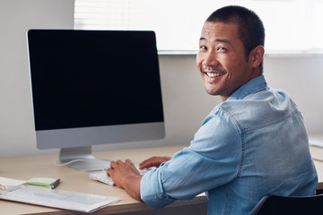 Happy young Asian entrepreneur at work on an office computer