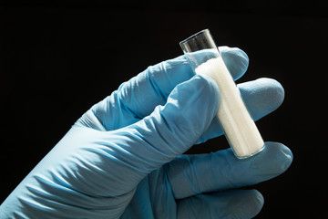 Wall Mural - Diabetes, a glass test tube with white sugar in the hands of a doctor in blue gloves on a black background, concept.