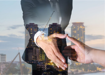 Double exposure of businessman will handshaking for business relationship, construction crane and building in the evening, twilight as industrial, commitment and partnership concept.