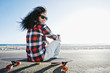 © Peathegee Inc/Blend Images - Hispanic woman sitting on skateboard at beach