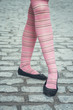 Female legs with pink trendy stripped tights and black ballerina flat shoes over a cobbled street, posing in a funny ballet step