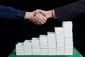 Businessman to shaking hand against the stacked of dollars