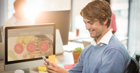 Poster - Smiling businessman using mobile phone at computer desk