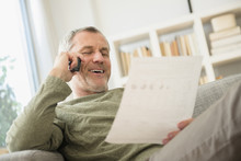 Older Caucasian Man Talking On Telephone Reading Paperwork