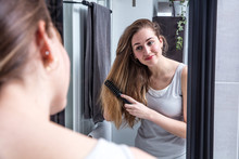 Attractive Young Woman Brushing Long Hair In Front Of Mirror