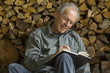 © Steve Smith/Blend Images - Caucasian man leaning on woodpile writing in journal