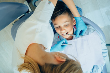 Female dentist very carefully check up and repair tooth of her young male patient.