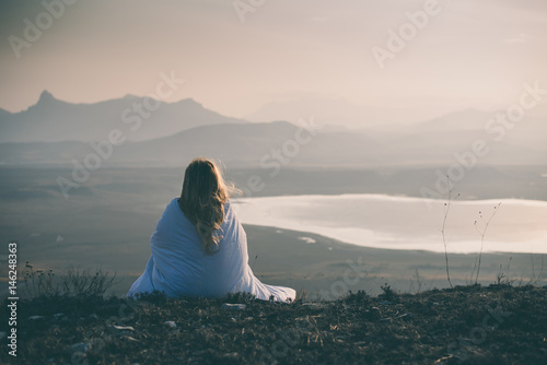Lonely sad and crying young woman sitting wrapped in blanket on cliff of mountain Poster