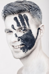 Wall Mural - Young man with black hand print on white face. Closeup Portrait.  Professional Fashion Makeup. fantasy art  makeup