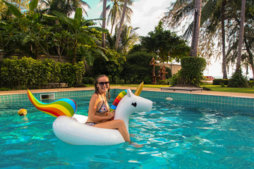 Young Caucasian Woman in Bikini Relaxing on Floating Unicorn in Swimming Pool