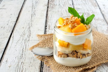 Wall Mural - tropical mango and pineapple parfait in a mason jar on a rustic white wood background