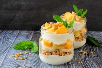 Wall Mural - tropical mango and pineapple parfaits in mason jars, scene on dark rustic background