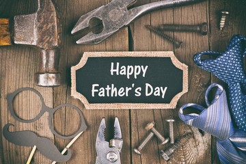 happy fathers day message on a chalkboard tag with frame of tools and ties on a wooden background, v