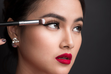 Close up of hand of asian woman applying eyeshadow on female eyelid.