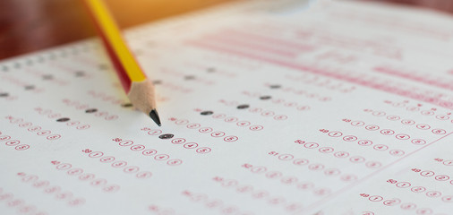 standardized test exams form with answers bubbled in and color pencil resting on the paper test, edu