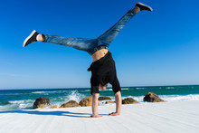 Young Athlete Doing Handstand On The Beach. Street Workout. Break Dancer Man Standing On Two Hands