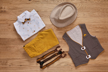 Top view photo of the boy's clothes with accessories on the wooden background.