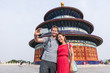 Happy couple travelers taking selfie picture together at temple of heaven during china summer travel. Young multiracial people using phone photography app for photos.