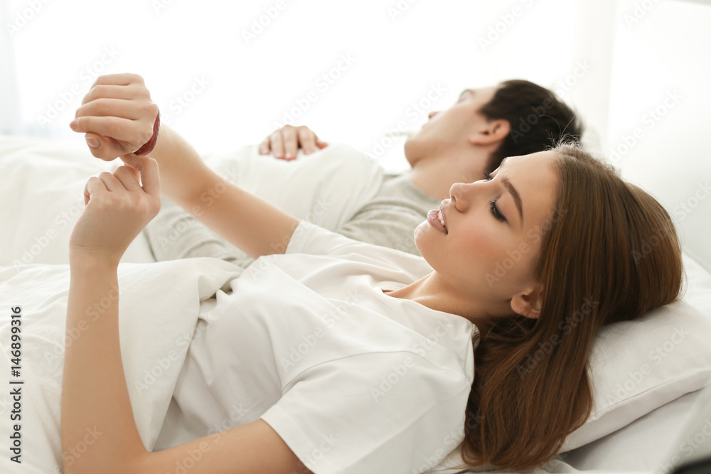 Beautiful young woman with sleep tracker lying in bed at home