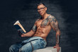 © Fxquadro - Shirtless muscular male with tattoo on a chest sits on a white wooden box and reads a book.