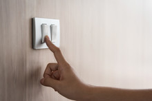 Close Up Hand Turning On Or Off On Grey Light Switch With Wooden Background. Copy Space.