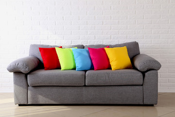 Colorful pillows on grey sofa on a brick wall background