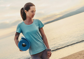 Wall Mural - Woman with yoga mat standing on beach