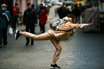 Woman in golden suit poses with raised hand and leg on the street